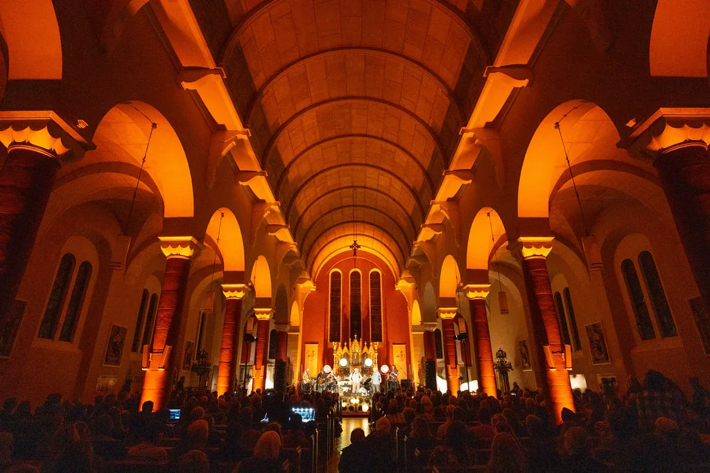 Grand interior of church lit with golden hues, audience seated for Mayo Dark Sky Festival event.